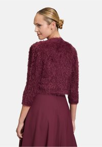 Veste courte texturée bordeaux en matériau doux, à manches trois-quarts et à col rond, associée à une jupe bordeaux.