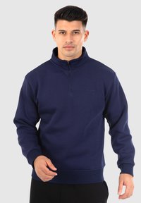 Felpa blu navy con colletto alto e chiusura a metà zip. Realizzata in tessuto morbido con polsini e orlo a costine, presenta un dettaglio logo sottile.
