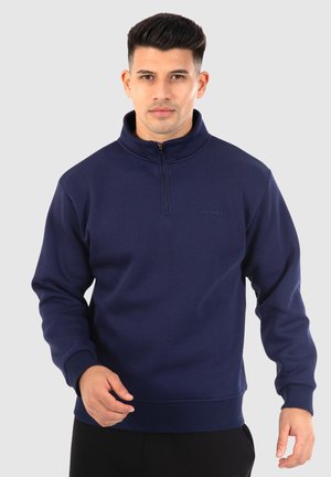 Felpa blu navy con colletto alto e chiusura a metà zip. Realizzata in tessuto morbido con polsini e orlo a costine, presenta un dettaglio logo sottile.