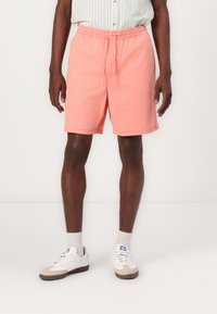 Lyserøde bomuldsshorts med elastisk talje og snor. Bæres med hvide og grå sneakers. Enkel design og knælængde.