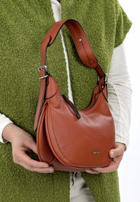 Sac à main en cuir marron avec une forme arrondie, une surface texturée, une fine bandoulière et des détails en métal argenté.