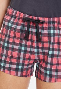 Pantalones cortos de cuadros rojos y marinos con cinturilla elástica, cordón negro y una textura de tela suave. Longitud corta y detalles de un patrón de cuadros clásico.