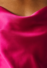 Gros plan de la partie supérieure de la poitrine d'une personne portant un vêtement en satin rose vif avec une texture lisse et brillante et la peau visible au-dessus de l'encolure.