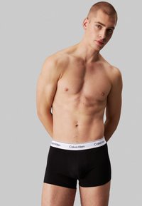 Boxers pretos ajustados com uma faixa branca que exibe o logótipo "Calvin Klein". O tecido parece suave e o design é justo, com um comprimento médio.