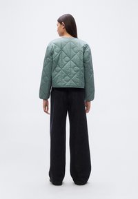 Πράσινο καπιτονέ μπουφάν με κοντό σχέδιο, διαθέτει στρογγυλή λαιμόκοψη και μακριά μανίκια, συνδυασμένο με σκούρο παντελόνι φαρδιάς γραμμής.