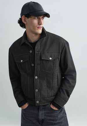 Melns denima jaka ar oranžām šuvēm, spiedpogu aizdare un divas krūšu kabatas. Valkāta virs melnas krekla un kombinēta ar tumšiem džinsiem.