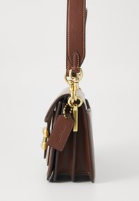 Brown leather handbag with a structured design, featuring gold-tone hardware, a detachable strap, and a tag with the brand name attached.