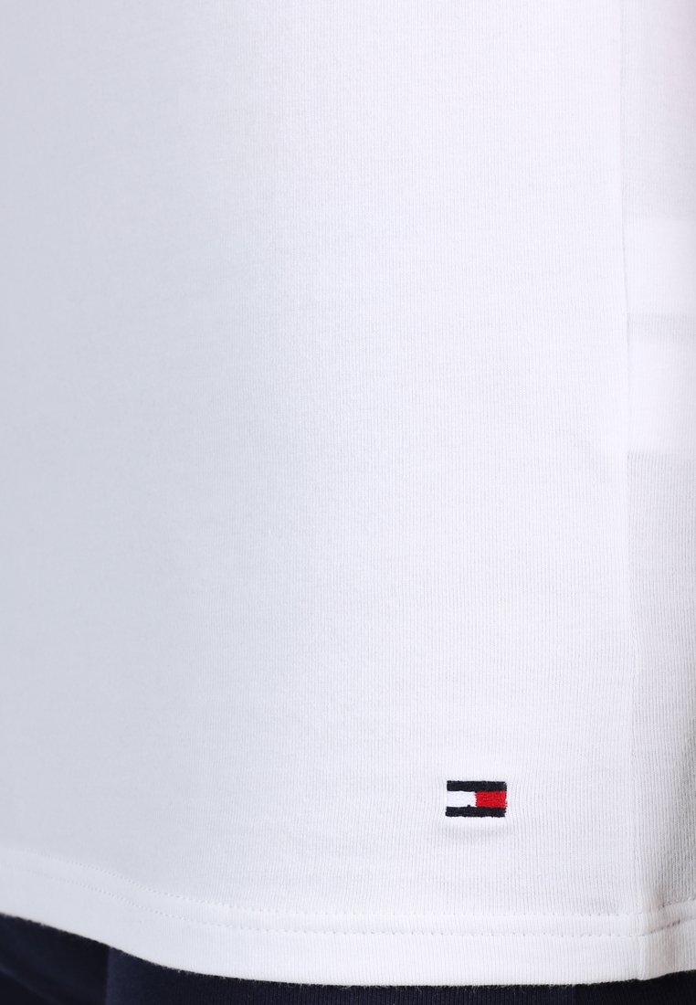 Weißes Baumwoll-T-Shirt mit rundem Ausschnitt, das am Saum ein kleines gesticktes Logo in Rot, Weiß und Blau aufweist. Weicher Stoff.