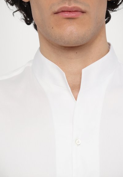 Hvit skjorte med ståkrage, laget av glatt stoff. Har en enkelt knappelukking ved halsen, med et minimalistisk design.