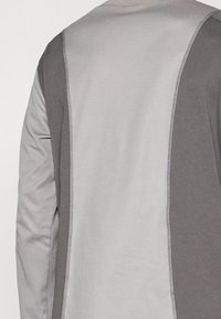 Gray long-sleeve shirt featuring a split design with light gray and medium gray panels, contrasting stitching along the seams, and a smooth texture.