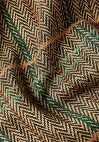 Textiel met een zigzagpatroon in zwart en beige, met accenten van groen en oranje. Zachte textuur, geweven stof met rijke details.