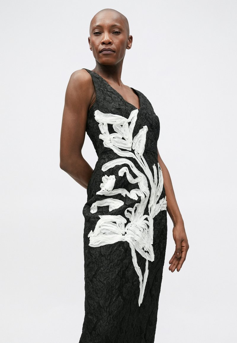Black sleeveless dress with textured fabric, featuring large white floral embellishments on the front in a flowing design.