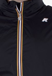 Schwarze Jacke mit mehrfarbigem gestreiften Reißverschluss und kleinem weißen und orangefarbenen Markenlogo auf der Brust.