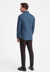 Camicia azzurra con bottoni e un sottile motivo a pois, abbinata a pantaloni scuri e scarpe nere, vista da dietro.
