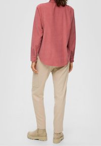 Roze langemouwen shirt met een afgeronde zoom, gecombineerd met beige broeken en tan enkellaarsjes. De broek heeft zijzakken.