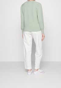 Maglione a maglia verde menta con design a coste, maniche a sbuffo e orlo aderente. Abbinato a pantaloni bianchi svasati e sneakers bianche.