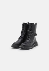Botas de combate de piel negra con puntera redonda, cordones en la parte delantera y detalle de hebilla. Presentan una marca en la suela y un exterior texturizado.