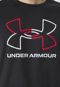 Sort bomulds t-shirt med et stort rødt og hvidt Under Armour logo-design; rund halsudskæring, korte ærmer, blød tekstur.