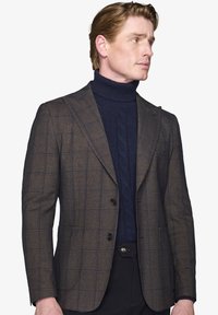 Brun ternet blazer med en skræddersyet pasform, to knapper og klapkrave. Bæres over en navy kabelstrik turtleneck. Glat uldblandingsstof.