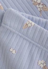 Ljusblå ribbad tyg med krämfärgade blommönster och beige blad, med synliga sömnadsdetaljer. Mjuk textur och mild färgpalett.