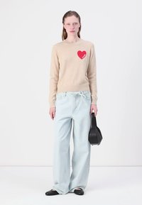 Beżowy sweter z czerwonym sercem, jasnoniebieskie szerokie spodnie, czarne baleriny i mała czarna torebka. Prosta, casualowa stylizacja.