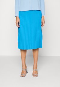 Falda midi plisada en azul brillante, hecha de tela ligera. Combinada con sandalias de tacón bloque de rayas multicolores con tiras en el tobillo.