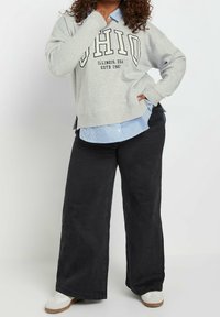 Grå sweatshirt med texten "OHIO", lagrad över en ljusblå randig skjorta med knappar. Svarta vida byxor och vita skor fulländar outfiten.