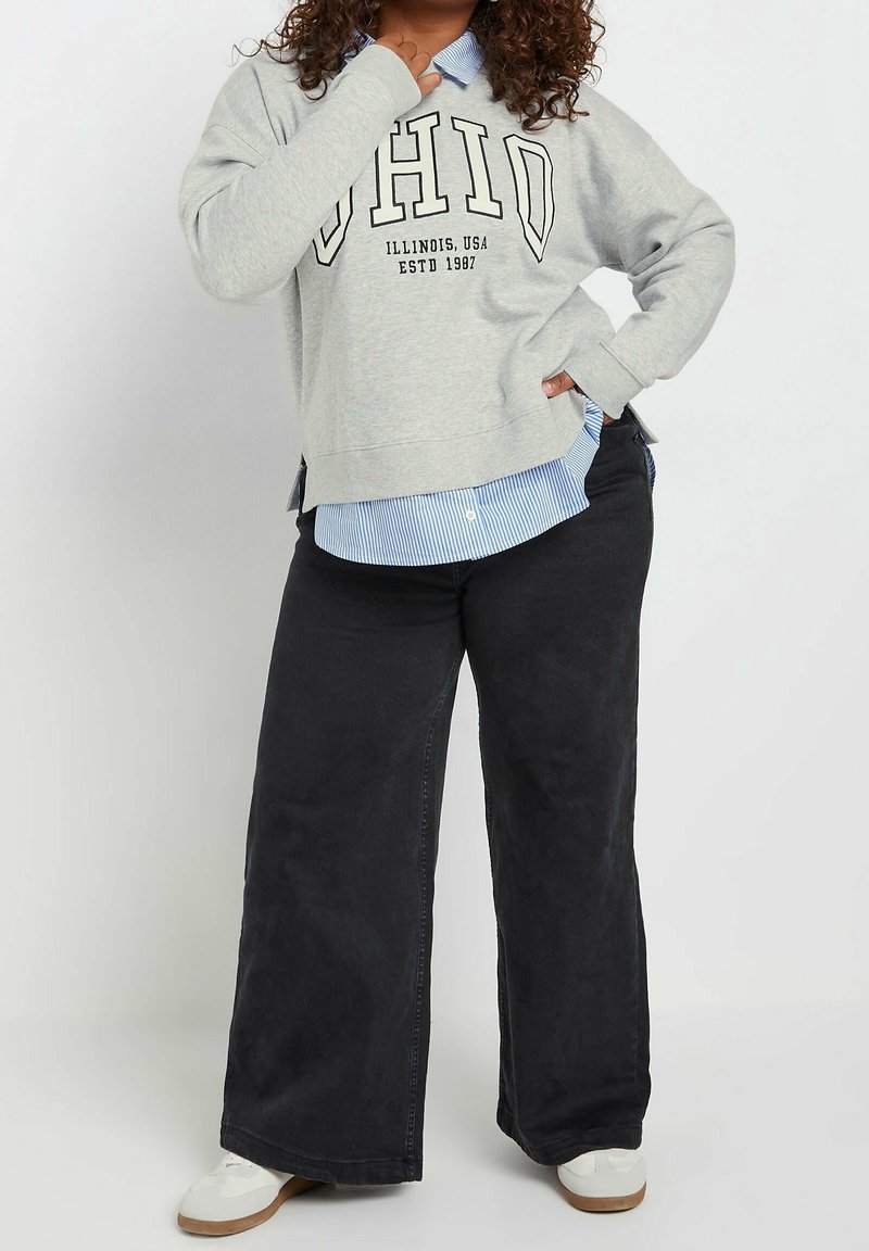 Grå sweatshirt med texten "OHIO", lagrad över en ljusblå randig skjorta med knappar. Svarta vida byxor och vita skor fulländar outfiten.