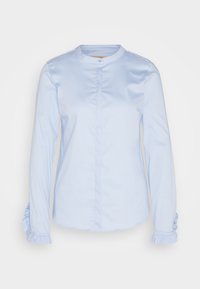 Blouse bleu clair à manches longues avec un col rond, des boutons cachés sur le devant et des poignets à volants aux manches.