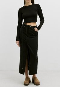 Zwarte geribbelde lange mouw cropped top gecombineerd met een zwarte denim rok met hoge taille en een split aan de voorkant, en bruine blokhak schoenen.