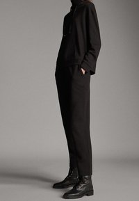 Mustat hupparit, joissa on nyöri, matching mustat kapeat housut ja mustat nauhalla varustetut saappaat, kaikki sileästä materiaalista. Yksinkertainen muotoilu.