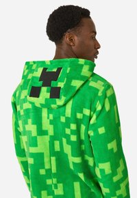 Green hooded sweatshirt made of soft, plush material, featuring pixelated patterns and a black logo on the back. Textured, vibrant appearance.