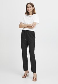 Zwarte joggerbroek met een trekkoord in de taille, taps toelopende benen en een gestructureerde stof, gecombineerd met een wit T-shirt en doorzichtige sandalen met hak.
