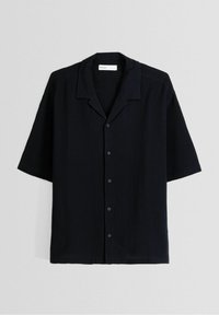 Lyhythihainen musta paita, joka on valmistettu teksturoidusta kankaasta. Paidassa on kauluksellinen pääntie, nappikiinnitys ja rento istuvuus.