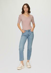 Haut à manches courtes côtelé rose clair, jeans droits bleus et baskets pâles avec des accents blancs. Le modèle se tient debout, les mains dans les poches.