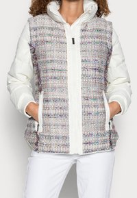 Chaleco de plumas con un frente de tela de tweed multicolor y lados acolchados blancos, que presenta un cierre de cremallera y bolsillos laterales.