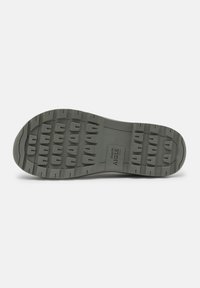 Semelle extérieure en caoutchouc gris avec un motif de semelle texturé, comportant de larges rainures et de petits crampons individuels pour une meilleure traction. Marquée du nom de la marque.