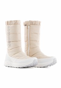 Beige gequiltte enkelboots met een witte zool, met een ritssluiting en een geraffineerde bovenkant. Merken weergegeven aan de zijkant in grijs.