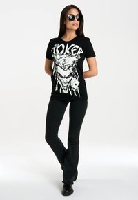 Black t-shirt featuring a large, white graphic of the Joker with purple accents. Paired with black flared pants and black shoes.