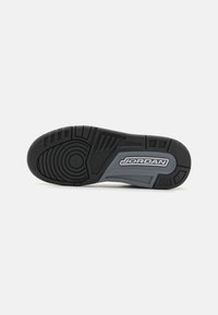 Semelle de sneaker en caoutchouc noir avec un motif de texture et un design circulaire. Comprend des accents gris et le logo "JORDAN" intégré sur le côté.