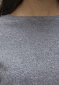 Szary dzianinowy top o gładkiej fakturze i szerokim dekolcie, z subtelnym, równomiernym wzorem na całej tkaninie.