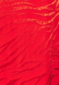 Tecido vermelho com um padrão texturizado em forma de onda, em um tom mais claro, apresentando acentos suaves e elevados que criam profundidade e interesse visual.