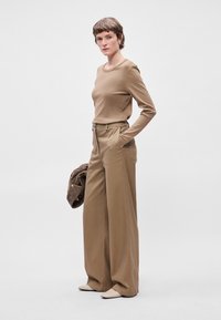 Καφέ μπλουζάκι με μακριά μανίκια, συνδυασμένο με ψηλόμεσο, φαρδύ παντελόνι σε ταιριαστό χρώμα. Απαλή υφή, μινιμαλιστικός σχεδιασμός και χωρίς ορατά μοτίβα.