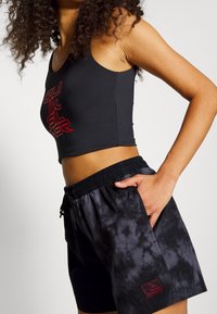 Černý krátký top s červeným logem, kombinovaný s tmavými šortkami s batikovým vzorem, elastickým pasem a boční kapsou.