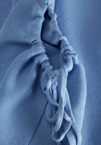 Jasnoniebieska dzianina z elastycznym detalem w formie marszczenia, o teksturowanym prążkowaniu i akcentach ze sznurkiem. Gładkie wykończenie i elastyczny materiał.