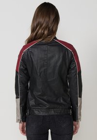 Giacca da moto in pelle nera con accenti a spalla in rosso trapuntato e pannelli laterali grigi, con zip sulle maniche e fasce laterali regolabili.