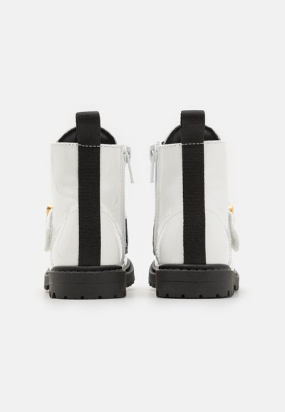 Valged patendinahk käärikinda saapad mustade elastsete külgpanelidega, tagumise tõmbluku abil ning tekstureeritud mustade kummitaldadega. Nähtav lukku sulgemine.