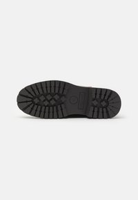Suela de goma negra con profundas huellas y surcos para tracción. Presenta un estampado de logo y tiene una forma redondeada. Adecuado para un uso robusto.