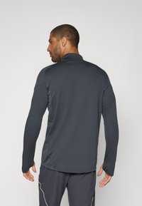 Langærmet atletisk top i mørkegrå stof, der har en høj krave, tætsiddende design og tommelfingerhuller ved manchetterne for ekstra funktionalitet.