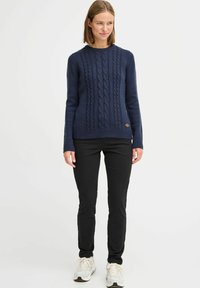 Navy cable-knit sweater with ribbed cuffs and hem, paired with black fitted pants and light-colored sneakers. Simple design, no patterns.